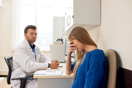 Upset woman covering face while talking to doctor