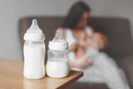 Bottles with breast milk on the background of mother holding in her hands and breastfeeding bab